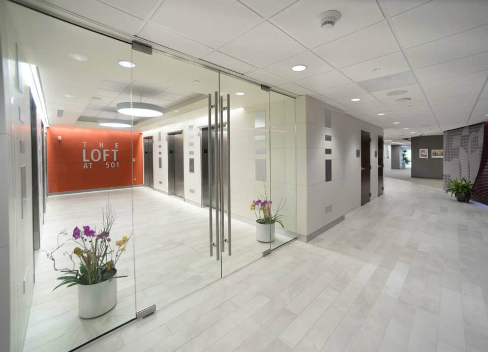 Modern office lobby entrance at The Loft at 501, featuring glass doors, decorative plants, and elevator access, reflecting Kazar's Electric's commercial electrical services.