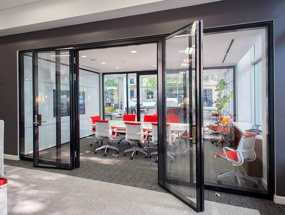 Modern conference room with glass doors, featuring red and white chairs, bright natural light, and a view of outdoor greenery, illustrating Kazar's Electric's commitment to professional environments.