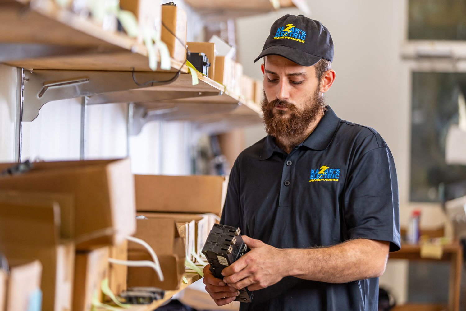 Kazar's Electric technician examining electrical components in a workshop, showcasing expertise in commercial electrical services.