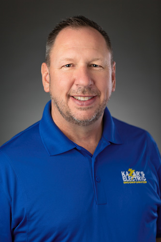 David Kazar, Owner of Kazar's Electric, smiles in a blue polo shirt against a professional grey background.