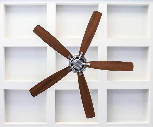 Modern ceiling fan with wooden blades by Kazar’s Electric, showcasing a minimalist design on a white grid wall.