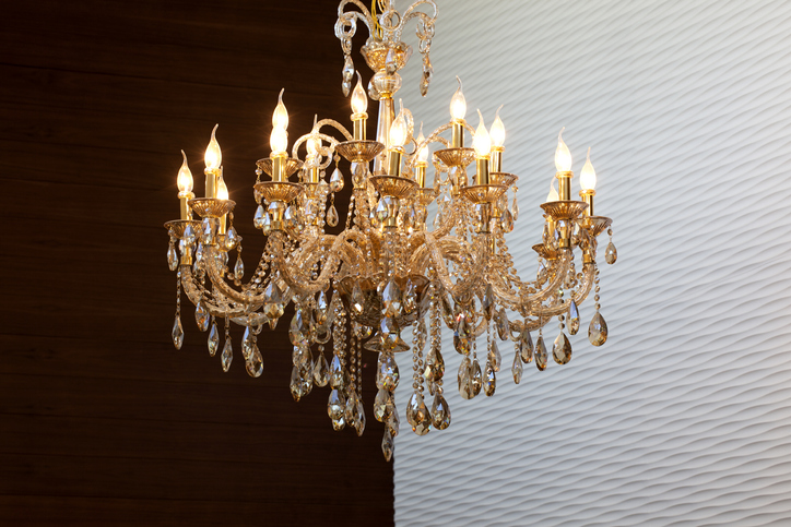 Elegant crystal chandelier by Kazar's Electric with intricate detailing and candle-style bulbs on a textured white wall.