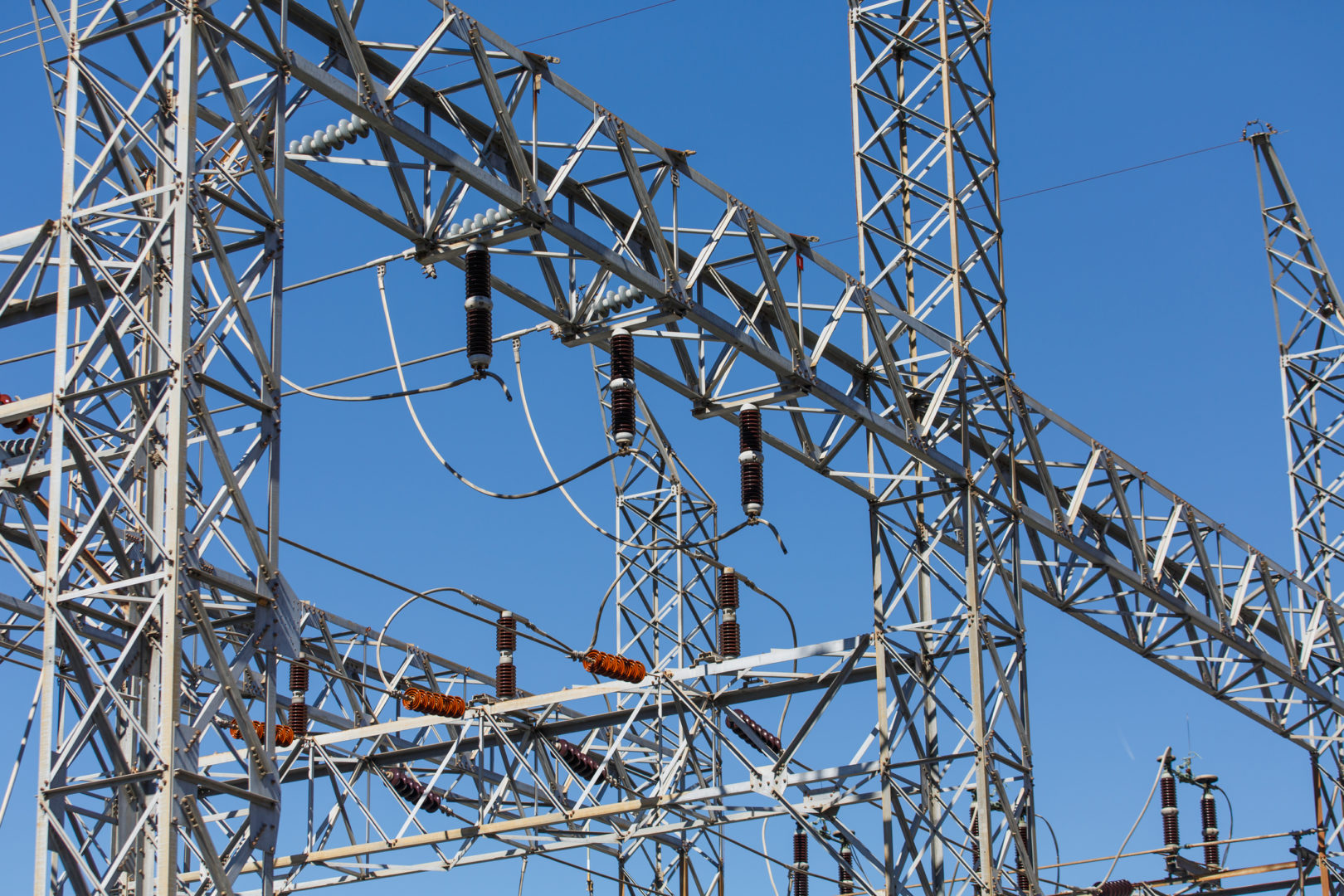 Electrical infrastructure with transmission towers, insulators, and cables under a clear blue sky, relevant to commercial surge protection services.