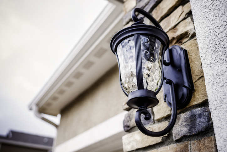 Exterior wall lantern light fixture with a decorative design, mounted on stone wall, enhancing home aesthetics and functionality.