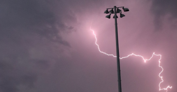 Lightning striking a pole under dark storm clouds, illustrating the importance of surge protection against electrical surges.