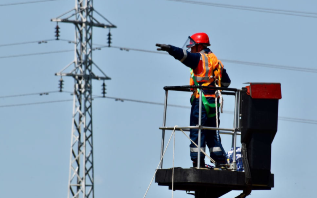Electrician in safety gear directing from a lift near power lines, emphasizing electrical services and energy efficiency.