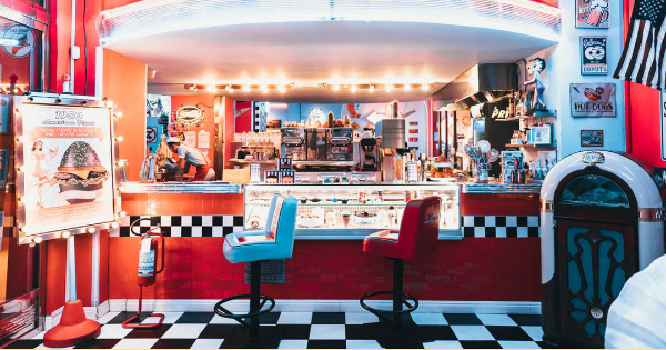 Retro diner interior with a checkered floor, colorful stools, illuminated counter, and vintage decor, illustrating an ideal restaurant environment for electrical work considerations.