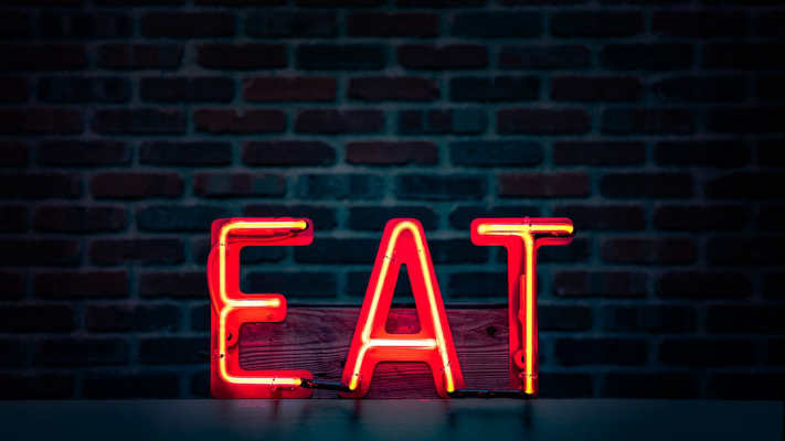 Neon sign spelling "EAT" in bright red against a dark brick wall, emphasizing the importance of restaurant ambiance and electrical services.
