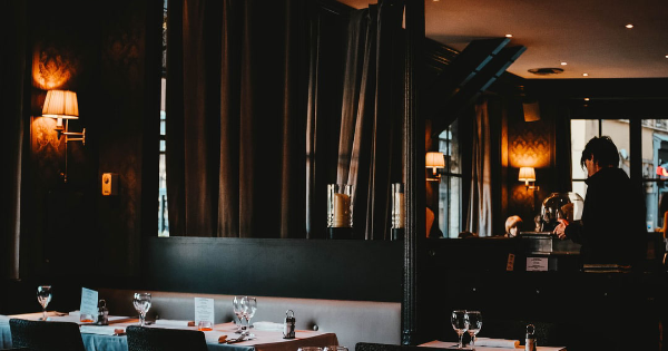 Elegant restaurant interior with tables set for dining, featuring soft lighting and a staff member preparing service, emphasizing the importance of electrical services for restaurant efficiency and safety.
