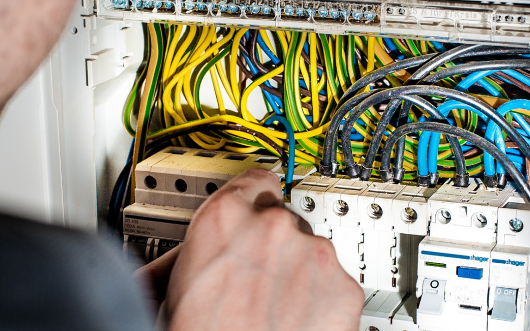 Close-up of a person working on an electrical panel, adjusting colorful wires and circuit breakers, emphasizing electrical upgrades for safety and compliance during home renovations.
