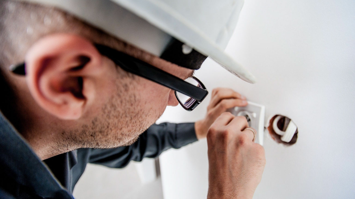 Electrician working on electrical outlet installation, wearing a hard hat and glasses, emphasizing the importance of skilled electrical contracting for construction projects.
