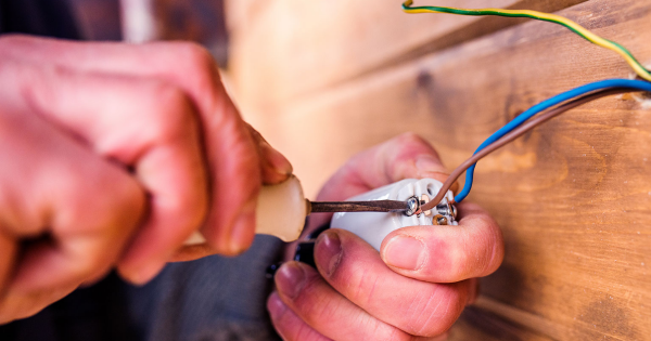 Person using a screwdriver to connect electrical wires to a junction box, illustrating hands-on electrical work relevant to National Electrical Code updates.