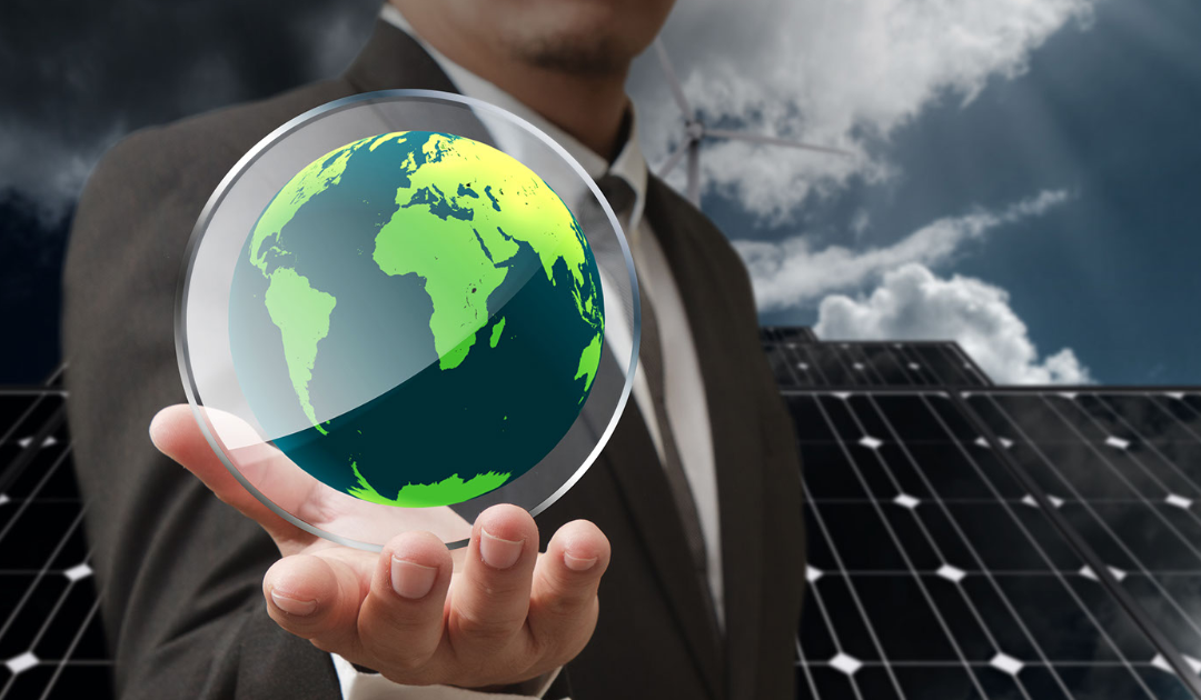 Businessman holding a transparent globe with a green Earth, set against a backdrop of solar panels and wind turbines, symbolizing energy efficiency and sustainability in commercial electrical systems.