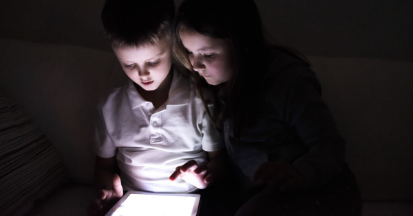 Children using a tablet in dim light, illustrating the importance of having electronic devices charged during a power outage.