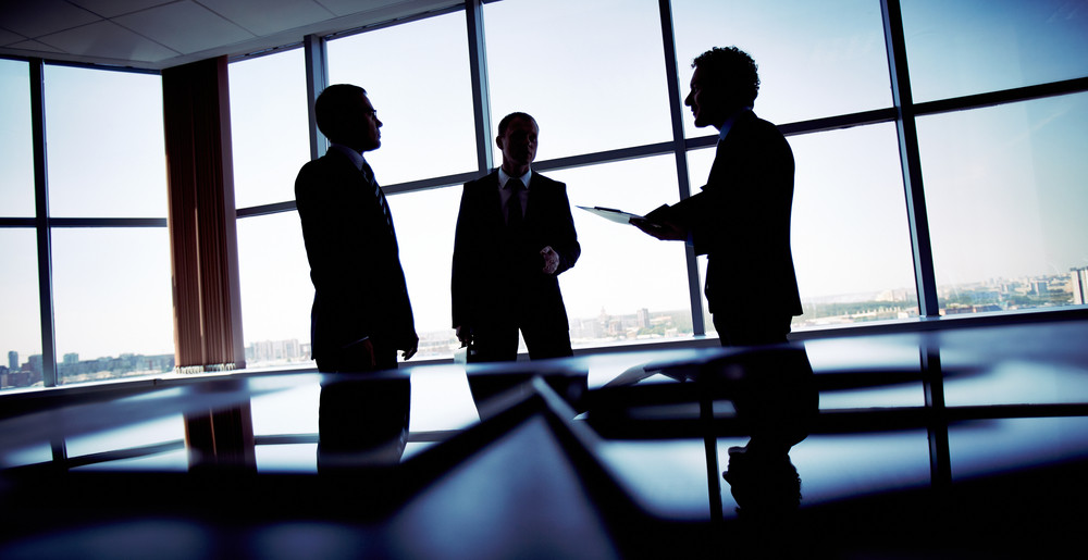 Business professionals discussing commercial electrical services in a modern office with large windows and city skyline view.