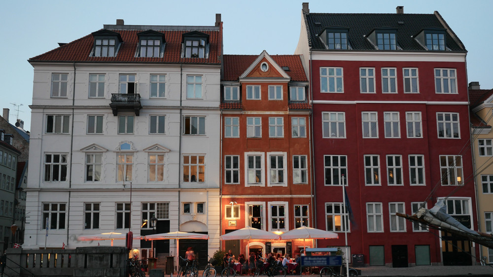 Colorful row of buildings in Copenhagen, showcasing a mix of architectural styles with outdoor dining and evening ambiance.