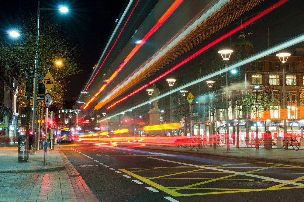 Parking lot illuminated at night with area lighting, showcasing vibrant light trails from passing vehicles, enhancing safety and visibility for pedestrians and drivers.