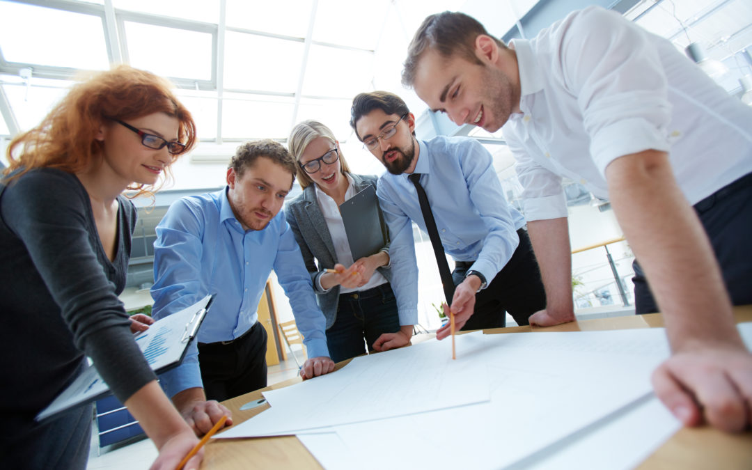 Group of professionals collaborating over architectural plans, emphasizing teamwork in electrical contracting projects.