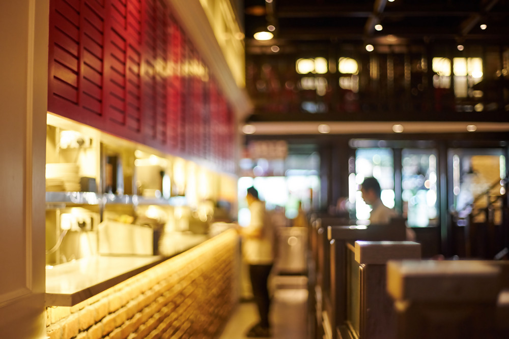 Restaurant interior with illuminated kitchen area, staff preparing food, and energy-efficient lighting, emphasizing electrical service importance for cost management.