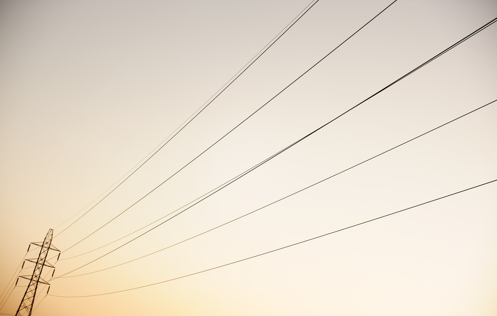 Electric power lines and a transmission tower against a gradient sky, symbolizing residential electrical services and energy-efficient lighting solutions.