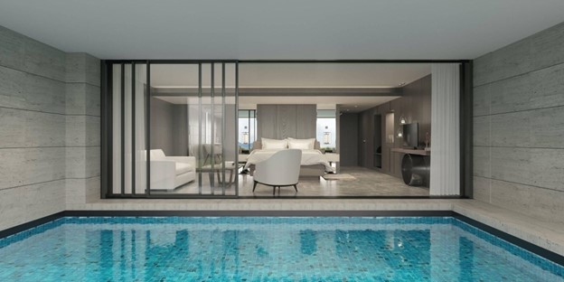 Indoor swimming pool with blue tiles reflecting light, adjacent to a modern living space featuring white furniture and large windows, emphasizing summer relaxation and pool maintenance.