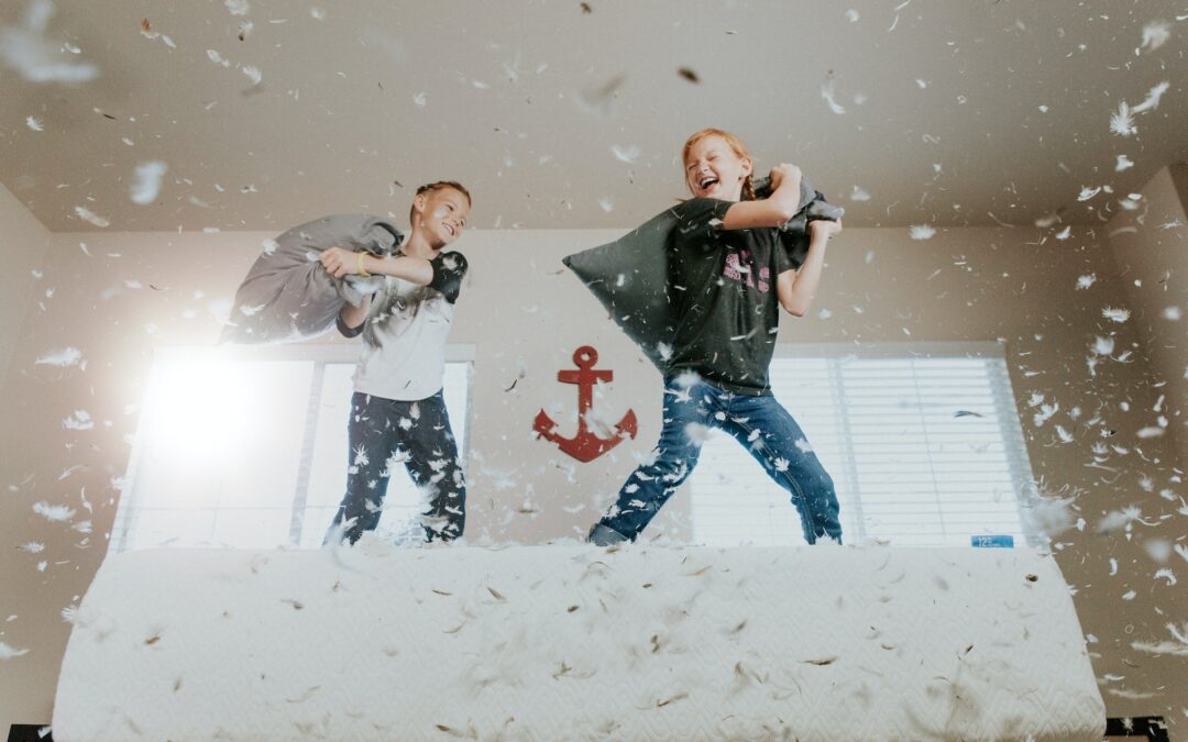 Children engaging in a playful pillow fight, surrounded by feathers in a bright room, emphasizing the importance of a safe and child-friendly environment.