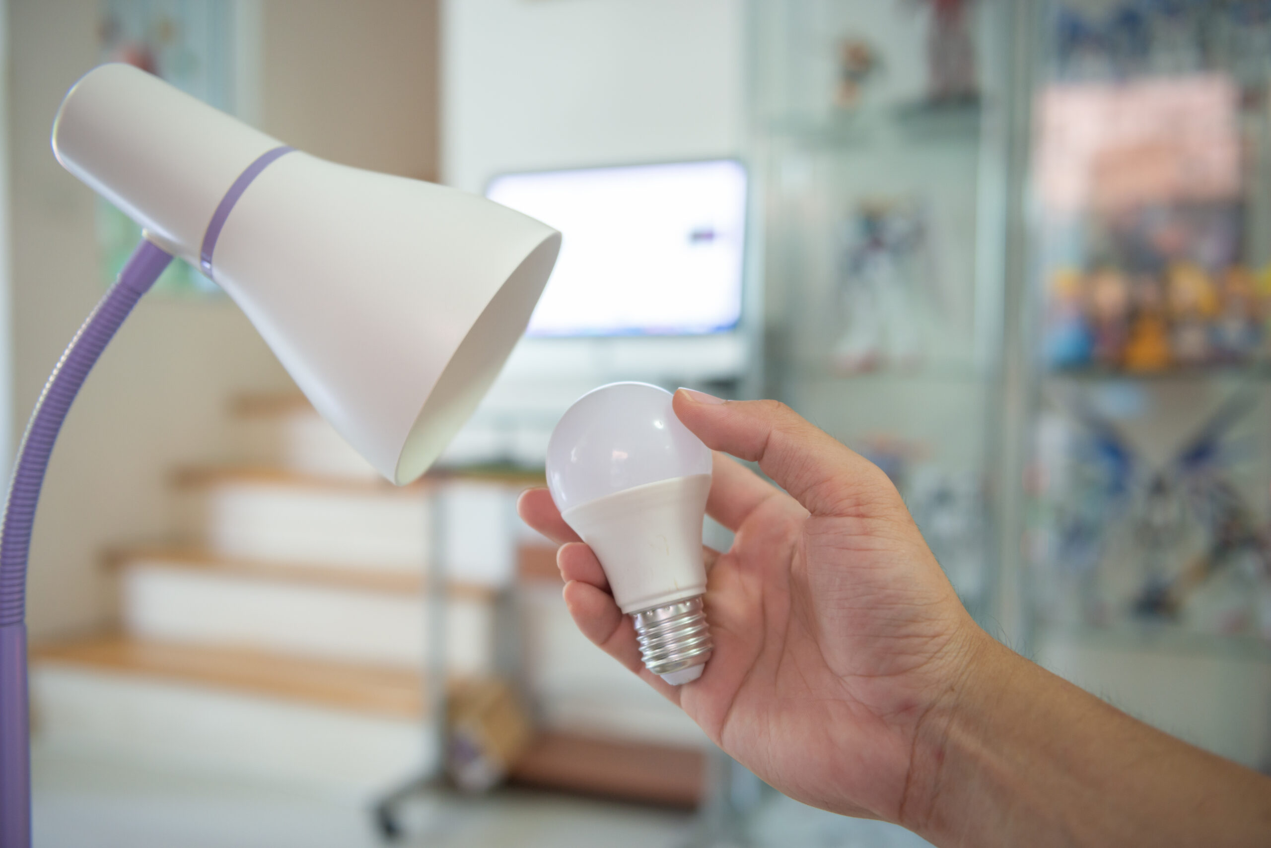 Person holding LED light bulb next to modern desk lamp in a home setting, illustrating energy-efficient lighting solutions for improved energy efficiency.