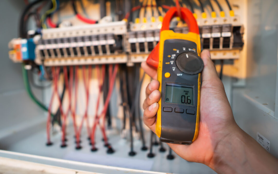 Hand holding a digital multimeter measuring current in an electrical panel, illustrating electrical safety and inspection relevant to home power systems during storms.