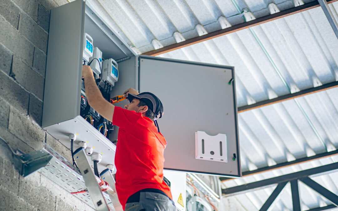 Electrician in red shirt working on commercial electrical panel, ensuring safe and reliable power systems for Tampa businesses.
