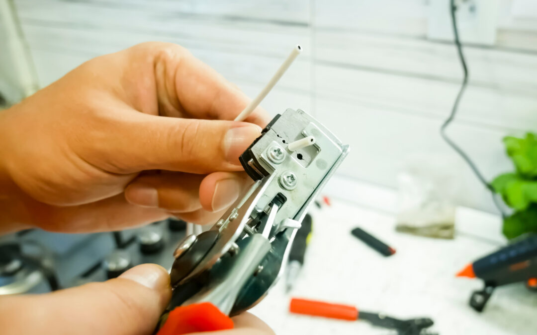Hands holding a wire stripper tool with a phone jack wire, demonstrating repair techniques relevant to phone jack maintenance and troubleshooting in homes.