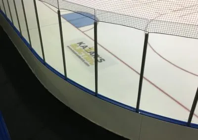 Professional ice rink with glass barriers and safety netting, showcasing Kazar's Electric's lighting installations.